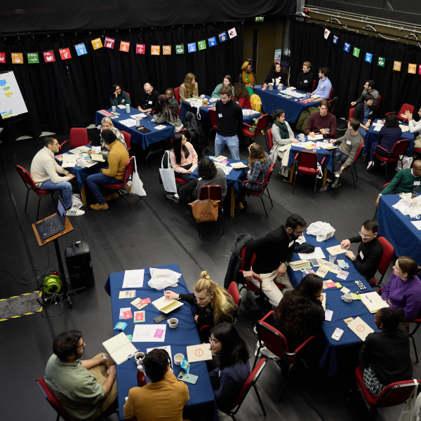 Teams of young people sat around desks working with coloured playing cards. There are SDGs banners all around the room.